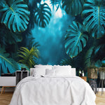 Papier Peint Panoramique Jungle Bleu dans une chambre à coucher apaisante avec lit blanc, table de chevet moderne, et plantes vertes. Illustration d'une forêt tropicale dense avec des feuilles de monstera luxuriantes et autres végétations, baignant dans une lumière douce et mystique.