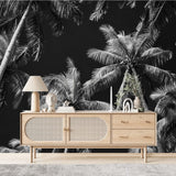 Papier Peint Panoramique Tropical Noir Et Blanc Exotique dans un salon de style scandinave avec buffet en bois clair et décoration minimaliste. Illustration d'une vue de contre-plongée de grands palmiers illuminés par une lumière douce avec un ciel nocturne en arrière-plan, créant une ambiance apaisante et sereine.