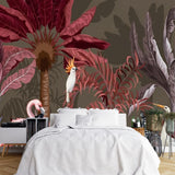 Papier Peint Action Jungle dans une chambre à coucher apaisante avec lit blanc, table de chevet moderne, et plantes vertes. Illustration d'une jungle tropicale luxuriante avec des flamants roses, un zèbre, un cacatoès blanc, et un héron entourés de grandes feuilles rouges et violettes sur un fond brun.