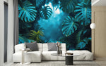 Papier Peint Panoramique Jungle Bleu dans un intérieur moderne et luxueux avec un grand canapé sectionnel blanc, une table basse en verre, et des touches dorées. Illustration d'une forêt tropicale dense avec des feuilles de monstera luxuriantes et autres végétations, baignant dans une lumière douce et mystique.