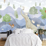 Papier Peint Elephant Enfant dans une chambre à coucher apaisante avec lit blanc, table de chevet moderne, et plantes vertes. Illustration d'un éléphant assis sur une colline entouré de lapins, d'un renard, de cerfs et d'oiseaux, avec un lapin flottant avec un parapluie, dans un style de livre pour enfants avec des teintes douces de bleu, vert, et beige.