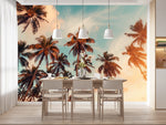 Tapisserie Plage Tropicale dans une salle à manger contemporaine avec table en bois naturel, chaises beiges et éclairage suspendu blanc. Illustration d'une scène tropicale au coucher du soleil avec des palmiers aux feuilles dorées et orangées, sur un ciel bleu, orange et rose pastel.