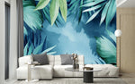 Tapisserie Jungle Vert Menthe dans un intérieur moderne et luxueux avec un grand canapé sectionnel blanc, une table basse en verre, et des touches dorées. Illustration de feuilles tropicales en style aquarelle sur un fond bleu, avec des palmiers et des monstera créant une ambiance apaisante et sereine.