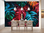 Papier Peint Tropical Coloré dans une salle à manger contemporaine avec table en bois naturel, chaises beiges et éclairage suspendu blanc. Illustration d'un motif vibrant de feuilles tropicales avec de grandes feuilles superposées aux détails minutieux, utilisant des couleurs rouges profonds, verts riches et oranges éclatants.