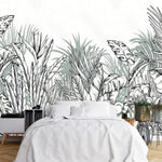 Papier Peint Panoramique Vegetal Noir Et Blanc dans une chambre à coucher apaisante avec lit blanc, table de chevet moderne, et plantes vertes. Illustration d'une dense jungle tropicale avec des feuilles luxuriantes et exotiques, dessinée au trait, incluant des feuilles de bananier, des palmiers et d'autres végétations tropicales distinctives dans une palette de nuances de vert et gris-vert doux.