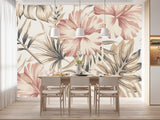 Papier Peint Imprimé Tropical Exotique dans une salle à manger contemporaine avec table en bois naturel, chaises beiges et éclairage suspendu blanc. Illustration d'un motif sophistiqué de feuilles tropicales et de fleurs d'hibiscus avec de grandes feuilles superposées et des détails minutieux, utilisant une palette de couleurs pastel composée de roses doux, crèmes et beige.