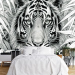 Papier Peint Noir Blanc Jungle Et Animaux dans une chambre à coucher apaisante avec lit blanc, table de chevet moderne, et plantes vertes. Illustration en noir et blanc d'un tigre au milieu de la jungle entouré de feuilles tropicales détaillées.