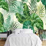 Tapisserie Tropicale Bananier dans une chambre à coucher apaisante avec lit blanc, table de chevet moderne, et plantes vertes. Illustration numérique de feuilles exotiques de monstera, bananiers, et palmiers avec une palette de différentes nuances de vert et beige en arrière-plan.