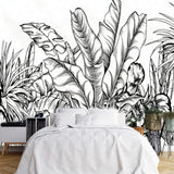 Papier Peint Vegetation Noir Et Blanc dans une chambre à coucher apaisante avec lit blanc, table de chevet moderne, et plantes vertes. Illustration d'un ensemble dense de plantes tropicales, avec des éléments végétaux tels que des feuilles de bananier et des fougères, en dessin à l'encre noir sur fond blanc.