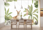 Papier Peint Animaux Jungle Exotique dans une salle à manger contemporaine avec table en bois naturel, chaises beiges et éclairage suspendu blanc. Illustration d'une scène tropicale australienne avec un koala, un kangourou, un dingo, et un diable de Tasmanie au premier plan, entourés de cacatoès, de perruches vertes, et d'un kookaburra parmi des palmiers et des plantes tropicales.