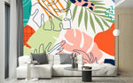 Papier Peint Jungle Panoramique Couleur dans un intérieur moderne et luxueux avec un grand canapé sectionnel blanc, une table basse en verre, et des touches dorées. Illustration d'art abstrait avec des motifs de feuilles tropicales dans différentes formes et couleurs, y compris vert, orange, rose, bleu marine, lavande, et blanc cassé, sur un fond blanc.