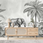 Papier Peint Chambre Enfant Jungle Noir Et Blanc dans un salon de style scandinave avec buffet en bois clair et décoration minimaliste. Illustration d'un éléphant marchant dans une jungle luxuriante avec des montagnes en arrière-plan, entouré de palmiers et de plantes tropicales en style gravure monochrome.