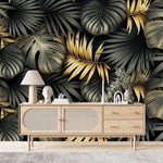 Papier Peint Tropical Noir Doré dans un salon de style scandinave avec buffet en bois clair et décoration minimaliste. Illustration d'un motif luxueux de feuilles tropicales avec de grandes feuilles superposées et des détails minutieux, utilisant des couleurs noir et or avec des textures contrastantes sur un fond sombre.