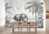 Papier Peint Chambre Enfant Jungle Noir Et Blanc dans une salle à manger contemporaine avec table en bois naturel, chaises beiges et éclairage suspendu blanc. Illustration d'un éléphant marchant dans une jungle luxuriante avec des montagnes en arrière-plan, entouré de palmiers et de plantes tropicales en style gravure monochrome.