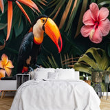 Papier Peint Panoramique Tropical Feuille Fleur Toucan Toucan et fleurs exotiques dans un cadre tropical luxuriant dans une chambre à coucher apaisante avec lit blanc, table de chevet moderne, et plantes vertes. 