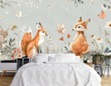 Papier Peint Animaux Foret Bebe dans une chambre à coucher apaisante avec lit blanc, table de chevet moderne, et plantes vertes. Illustration d'un lapin et de deux renards dans une forêt magique, entourés de fleurs délicates et de papillons colorés, avec une palette de couleurs pastel douce.