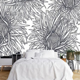 Papier Peint Vegetal Noir Et Blanc dans une chambre à coucher apaisante avec lit blanc, table de chevet moderne, et plantes vertes. Illustration de motifs floraux stylisés en noir et blanc avec des fleurs exotiques aux pétales allongés, dessinées de manière symétrique en style de dessin au trait.