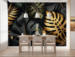 Papier Peint Tropical Noir dans une salle à manger contemporaine avec table en bois naturel, chaises beiges et éclairage suspendu blanc. Illustration d'un motif luxueux de feuilles tropicales avec de grandes feuilles superposées et des détails minutieux, utilisant des couleurs noir et or avec des textures contrastantes sur un fond sombre.