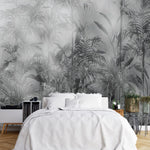 Papier Peint Noir Et Blanc Motif Vegetal dans une chambre à coucher apaisante avec lit blanc, table de chevet moderne, et plantes vertes. Illustration d'une jungle dense et brumeuse avec des plantes tropicales luxuriantes et des oiseaux cachés parmi les branches, réalisée dans une palette de gris et verts foncés.