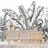 Papier Peint Tropical Fond Blanc Exotique dans un salon de style scandinave avec buffet en bois clair et décoration minimaliste. Illustration d'un motif détaillé de feuilles tropicales avec de grandes feuilles superposées et un travail de lignes minutieux, réalisée dans un style noir et blanc.