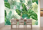 Tapisserie Tropicale Bananier dans une salle à manger contemporaine avec table en bois naturel, chaises beiges et éclairage suspendu blanc. Illustration numérique de feuilles exotiques de monstera, bananiers, et palmiers avec une palette de différentes nuances de vert et beige en arrière-plan.