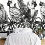 Papier Peint Jungle Noir Et Blanc Perroquet dans une chambre à coucher apaisante avec lit blanc, table de chevet moderne, et plantes vertes. Illustration monochrome de quatre perroquets perchés sur des feuilles tropicales, réalisée en nuances de noir et blanc avec des détails sophistiqués.