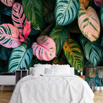 Papier Peint Feuillage Tropical Exotique dans une chambre à coucher apaisante avec lit blanc, table de chevet moderne, et plantes vertes. Illustration d'un motif vibrant de feuilles tropicales avec de grandes feuilles superposées et des détails minutieux, utilisant des couleurs roses, verts et oranges avec des motifs et textures variés.