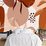 Papier Peint Panoramique Jungle Terracotta dans une chambre à coucher apaisante avec lit blanc, table de chevet moderne, et plantes vertes. Illustration abstraite avec formes géométriques et motifs de feuilles stylisés dans des tons de marron, beige, et terre cuite.