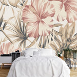 Papier Peint Imprimé Tropical Exotique dans une chambre à coucher apaisante avec lit blanc, table de chevet moderne, et plantes vertes. Illustration d'un motif sophistiqué de feuilles tropicales et de fleurs d'hibiscus avec de grandes feuilles superposées et des détails minutieux, utilisant une palette de couleurs pastel composée de roses doux, crèmes et beige.