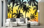 Papier Peint Panoramique Jungle Action dans un intérieur moderne et luxueux avec un grand canapé sectionnel blanc, une table basse en verre, et des touches dorées. Illustration d'une scène tropicale au coucher du soleil avec des silhouettes de palmiers en noir, sur un fond dégradé de bleu, jaune, orange et rouge.