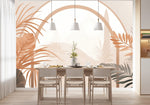 Papier Peint Panoramique Jungle Sepia Tropical dans une salle à manger contemporaine avec table en bois naturel, chaises beiges et éclairage suspendu blanc. Illustration numérique minimaliste représentant une scène tropicale avec un arrière-plan montagneux et des cadres architecturaux semi-circulaires, incluant des plantes tropicales comme des palmiers et des feuilles de monstera, dans des tons beige, marron et ocre. 