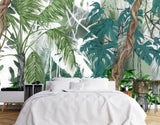 Papier Peint Panoramique Safari dans une chambre à coucher apaisante avec lit blanc, table de chevet moderne, et plantes vertes. Illustration d'une scène tropicale dense avec des plantes aux grandes feuilles vertes, des lianes brunes et un fond flou en nuances de vert, blanc et gris, montrant une forêt épaisse.