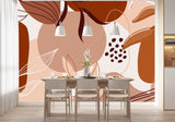 Papier Peint Panoramique Jungle Terracotta dans une salle à manger contemporaine avec table en bois naturel, chaises beiges et éclairage suspendu blanc. Illustration abstraite avec formes géométriques et motifs de feuilles stylisés dans des tons de marron, beige, et terre cuite.