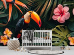 Papier Peint Panoramique Tropical Feuille Fleur Toucan dans une chambre de bébé moderne et minimaliste avec des murs blancs et un sol foncé, un berceau blanc, une couverture grise à pompons, des peluches, des jouets en bois et un tapis à motif noir et blanc. Illustration d'un toucan coloré perché sur une branche au milieu de feuillages tropicaux verts épais, entouré de fleurs exotiques telles que des hibiscus roses et des fleurs de frangipanier jaunes.