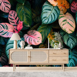 Papier Peint Feuillage Tropical Exotique dans un salon de style scandinave avec buffet en bois clair et décoration minimaliste. Illustration d'un motif vibrant de feuilles tropicales avec de grandes feuilles superposées et des détails minutieux, utilisant des couleurs roses, verts et oranges avec des motifs et textures variés.