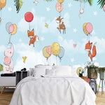 Papier Peint Bébé Elephant dans une chambre à coucher apaisante avec lit blanc, table de chevet moderne, et plantes vertes. Illustration d'un ciel d'été avec des animaux mignons accrochés à des ballons colorés, comprenant des éléphants, cerfs, hérissons, renards et lapins, flottant parmi des nuages et des étoiles avec une guirlande de fanions en dessous.