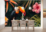 Papier Peint Panoramique Tropical Feuille Fleur Toucan dans une salle à manger contemporaine avec table en bois naturel, chaises beiges et éclairage suspendu blanc. Illustration d'un toucan coloré perché sur une branche au milieu de feuillages tropicaux verts épais, entouré de fleurs exotiques telles que des hibiscus roses et des fleurs de frangipanier jaunes.