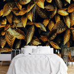 Papier Peint Panoramique Tropical Jungle dans une chambre à coucher apaisante avec lit blanc, table de chevet moderne, et plantes vertes. Illustration de feuilles dorées et brunes aux textures détaillées et aux bords dentelés, étalées de manière aléatoire, avec un contraste intense entre les couleurs chaudes et les zones d'ombre.