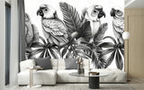 Papier Peint Jungle Noir Et Blanc Perroquet dans un intérieur moderne et luxueux avec un grand canapé sectionnel blanc, une table basse en verre, et des touches dorées. Illustration monochrome de quatre perroquets perchés sur des feuilles tropicales, réalisée en nuances de noir et blanc avec des détails sophistiqués.