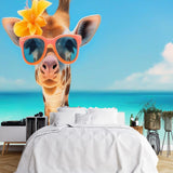 Papier Peint Theme Safari dans une chambre à coucher apaisante avec lit blanc, table de chevet moderne, et plantes vertes. Illustration d'une girafe portant des lunettes de soleil roses et une fleur jaune sur la tête, se tenant sur une plage tropicale avec une mer turquoise et un ciel bleu clair.