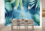 Tapisserie Jungle Vert Menthe dans une salle à manger contemporaine avec table en bois naturel, chaises beiges et éclairage suspendu blanc. Illustration de feuilles tropicales en style aquarelle sur un fond bleu, avec des palmiers et des monstera créant une ambiance apaisante et sereine.