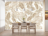 Papier Peint Jungle Action dans une salle à manger contemporaine avec table en bois naturel, chaises beiges et éclairage suspendu blanc. Illustration d'un motif de feuilles tropicales avec de grandes feuilles superposées et des détails minutieux, utilisant une palette de couleurs monochromatique de diverses nuances de beige.