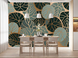 Papier Peint Tropical Chic Exotique dans une salle à manger contemporaine avec table en bois naturel, chaises beiges et éclairage suspendu blanc. Illustration d'un motif moderne de feuilles tropicales avec des feuilles superposées et des détails de nervures complexes, utilisant une palette de couleurs composée de verts foncés, bleus et ors.