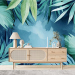 Tapisserie Jungle Vert Menthe dans un salon de style scandinave avec buffet en bois clair et décoration minimaliste. Illustration de feuilles tropicales en style aquarelle sur un fond bleu, avec des palmiers et des monstera créant une ambiance apaisante et sereine.