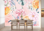 Papier Peint Tropical Cuisine dans une salle à manger contemporaine avec table en bois naturel, chaises beiges et éclairage suspendu blanc. Illustration d'un motif floral aquarelle, avec des fleurs roses et blanches éclatantes, des tranches d'orange, et des feuilles vert foncé sur un fond rose pastel.