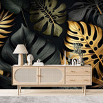 Papier Peint Tropical Noir dans un salon de style scandinave avec buffet en bois clair et décoration minimaliste. Illustration d'un motif luxueux de feuilles tropicales avec de grandes feuilles superposées et des détails minutieux, utilisant des couleurs noir et or avec des textures contrastantes sur un fond sombre.