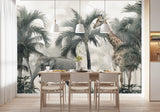 Tapisserie Paysage Tropicale dans une salle à manger contemporaine avec table en bois naturel, chaises beiges et éclairage suspendu blanc. Illustration d'un éléphant et d'une girafe parmi des palmiers dans une forêt tropicale.